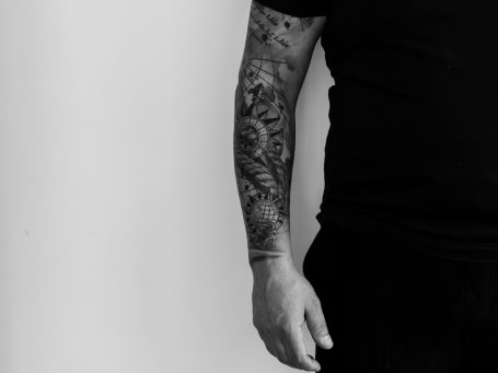 Ein Arm mit einem detaillierten, schwarzen Tattoo auf einem neutralen Hintergrund.
