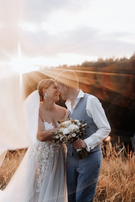 Braut und Bräutigam umarmen sich in einer sonnigen Wiese bei Sonnenuntergang.